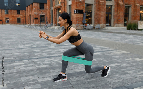 Athletic woman doing lunges exercise with a fitness elastic band outdoor