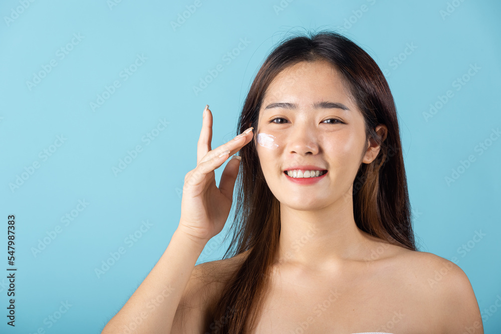 Skin care and beauty concept. young woman applying moisturizer cream on her face studio shot isolated on blue background, Happy beauty portrait female gets cream on her cheek, health clean skin Skin care and beauty concept. young woman applying moisturizer cream on her face studio shot isolated on blue background, Happy beauty portrait female gets cream on her cheek, health clean skin