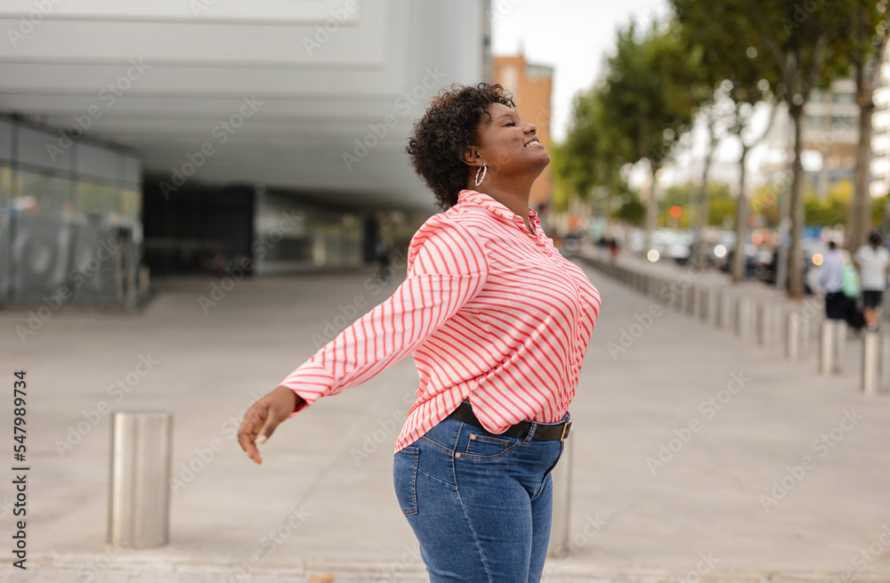 African american curvy woman opening her arms and closing her eyes relaxed in the middle of the city.