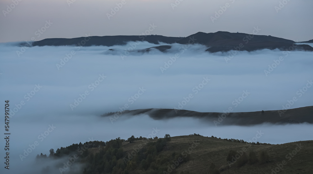 Clouds crawling up the mountain and absorbing it in themselves in the autumn mountains, on a twilight evening in the mountains of the Caucasus