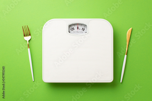 Weight loss concept. Top view photo of cutlery fork knife and scales on isolated green background