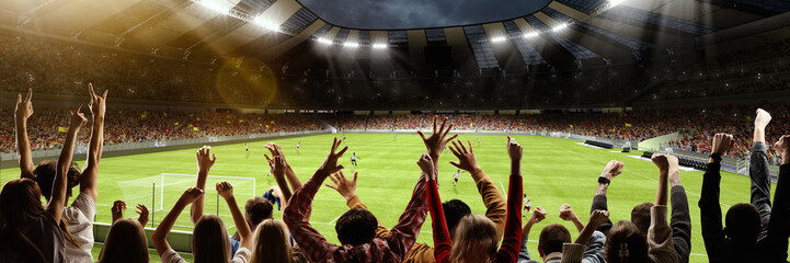 Back view of group of people, football soccer fans cheering at crowded football stadium at evening time. Concept of sport, cup, world, team, event, competition