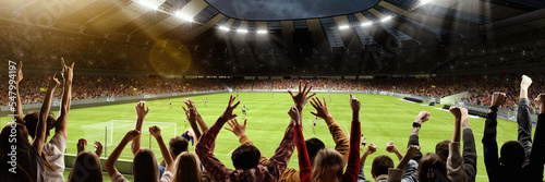 Back view of group of people, football soccer fans cheering at crowded football stadium at evening time. Concept of sport, cup, world, team, event, competition