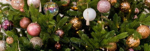 Gold Christmas ball on a Christmas tree in a light interior against the background of burning garlands of lights. Decorating Christmas tree Happy holidays. Web banner