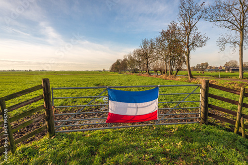 Inverted Dutch flag mounted on a gate in front of a muddy meadow in the Alblasserwaard region. This is happening in the context of the farmers' protest against government policy on nitrogen emissions.
