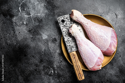 Fresh turkey legs Drumsticks, raw Poultry meat with butcher cleaver. Black background. Top view. Copy space