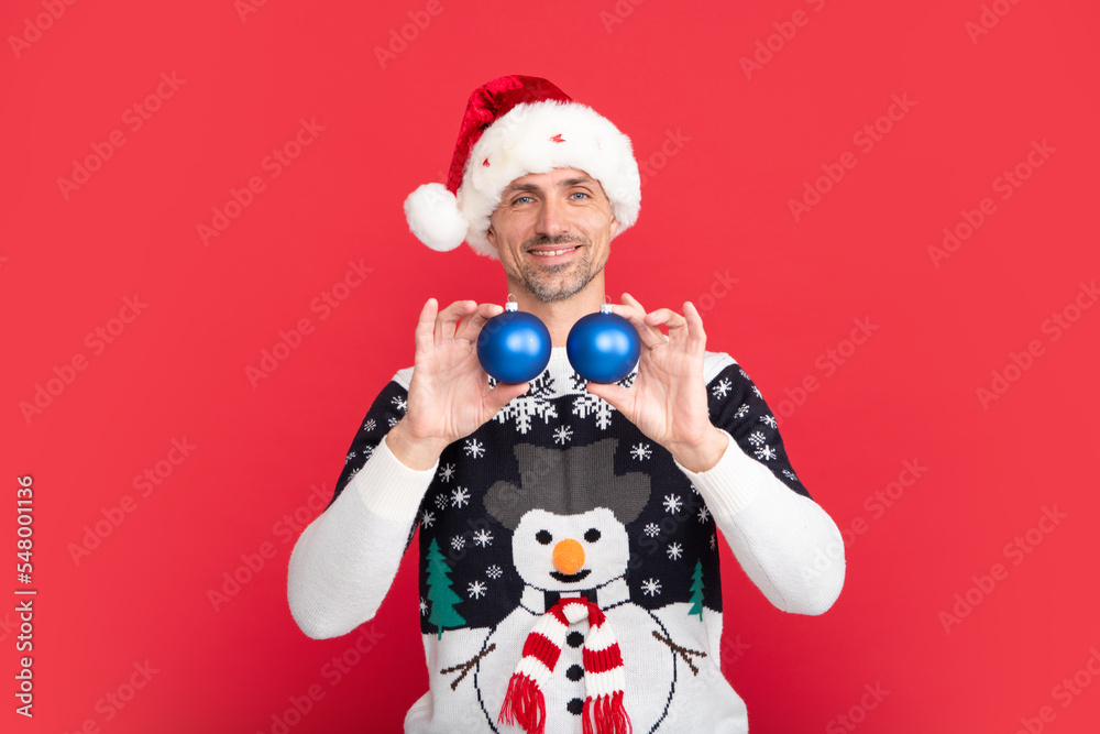 Man in Christmas sweater and Santa hat on red background. Santa with bauble, christmas ball.