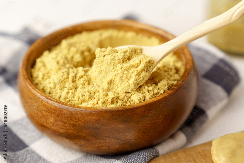 Mustard powder close up in a bowl on white table, selective focus. Mustard powder close up in a bowl on white table, selective focus.