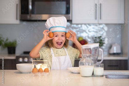 Child chef cook with eggs. Kid chef cook in chef hat preparing food on kitchen. Child making tasty delicious. Cooking meal.