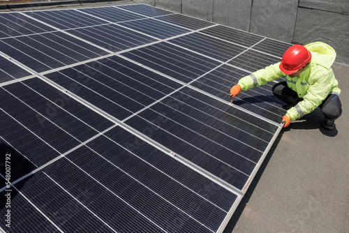 operaio con caschetto protettivo rosso , tuta specialistica e occhiali tecnici lavora su un impianto fotovoltaico istallato sul tetto di un edificio photo