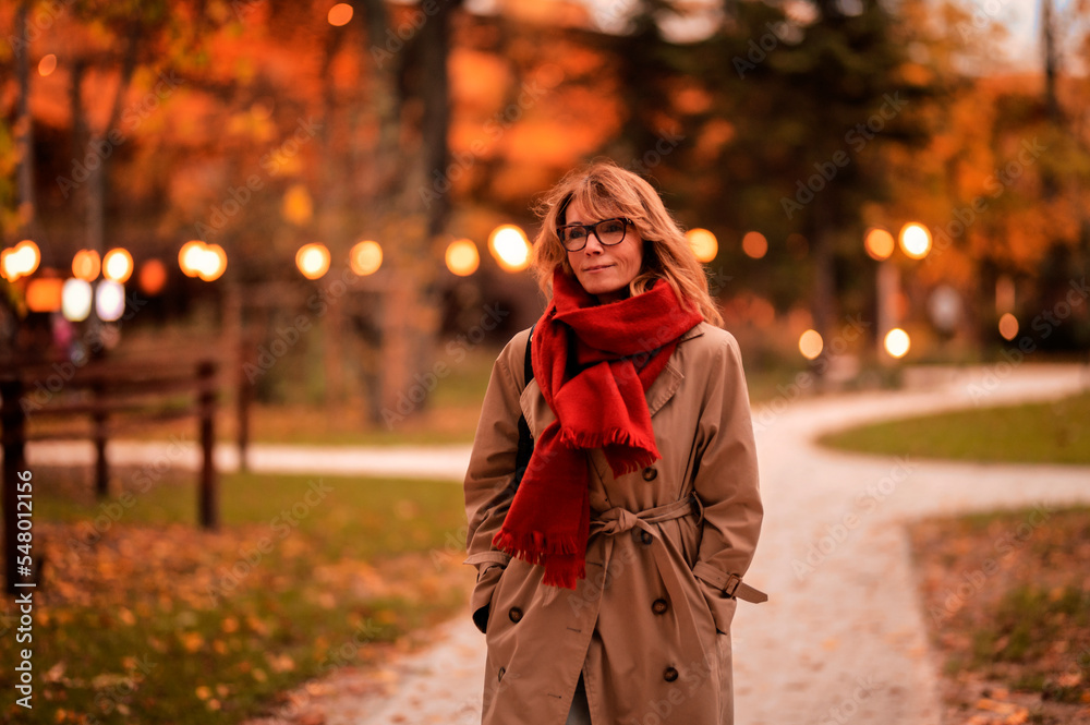 Fashionable middle aged woman walking in the street and enjoying autumn afternoon. Attractive female wearing scarf and trench coat outdoor. Fashionable middle aged woman walking in the street and enjoying autumn afternoon. Attractive female wearing scarf and trench coat outdoor.