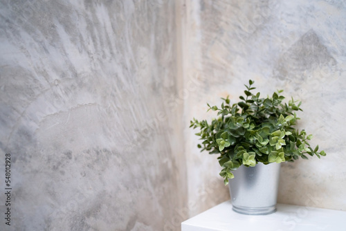 Artificial plant in steel pot on white shelf with concrete background