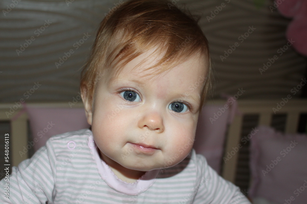 Cute little girl standing in the crib and looking at the camera