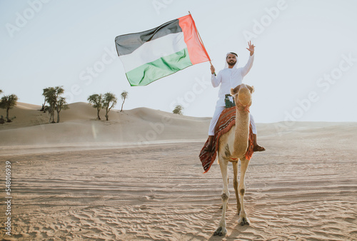 Man wearing traditional clothes, taking a camel out on the desert sand, in Dubai
