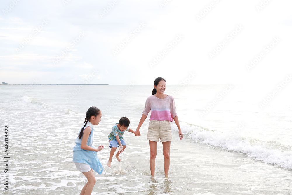 Happy family mom and child having fun in summer holiday. Asian mother and kids enjoy playing on tropical sand beach at sunrise.