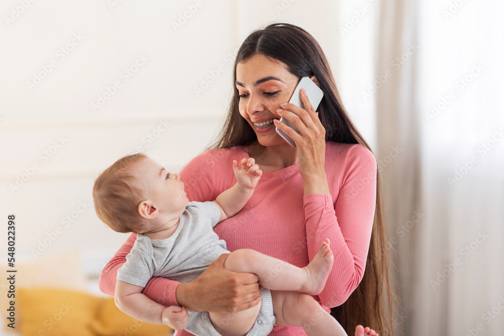 Young mother's lifestyle concept. Happy mom talking on cellphone, holding baby in arms and having phone conversation Young mother's lifestyle concept. Happy mom talking on cellphone, holding baby in arms and having phone conversation