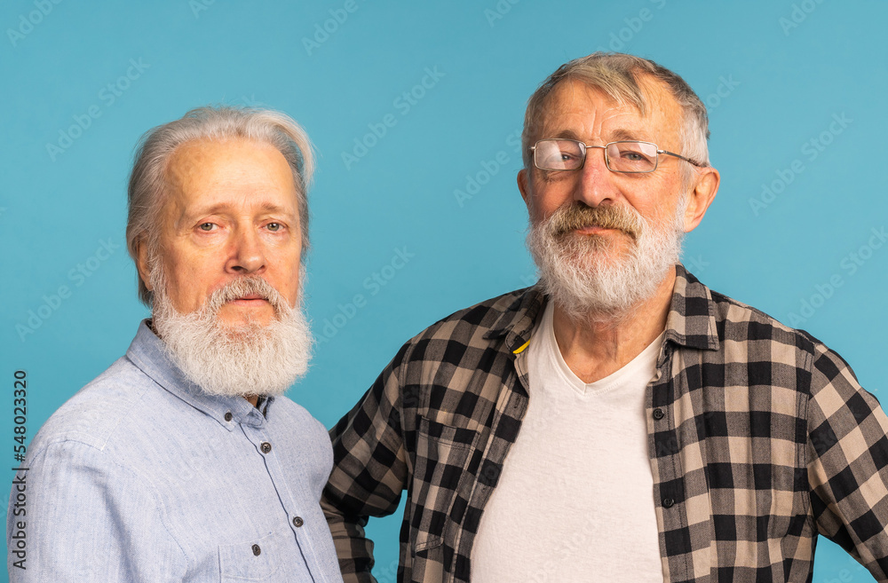 Portrait two elderly man friends standing over blue background - friendship, aged and senior people Portrait two elderly man friends standing over blue background - friendship, aged and senior people