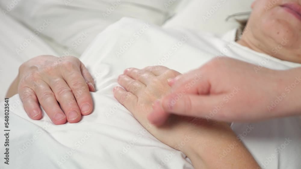 Daughter strokes hand of sick mother lying in bed at home. Woman takes care of elderly bedridden mom after difficult surgery showing support closeup Daughter strokes hand of sick mother lying in bed at home. Woman takes care of elderly bedridden mom after difficult surgery showing support closeup
