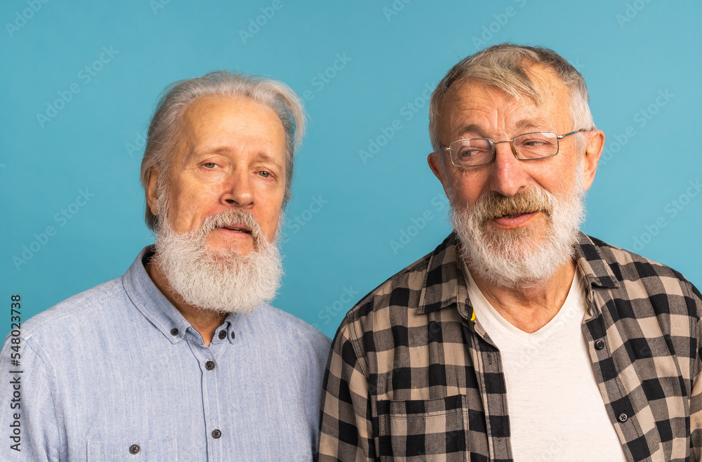 Portrait two elderly man friends standing over blue background - friendship, aged and senior people Portrait two elderly man friends standing over blue background - friendship, aged and senior people