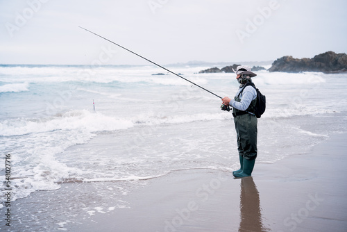 latin woman with a fishing rod and fisherman outfit on the shore of the beach fishing