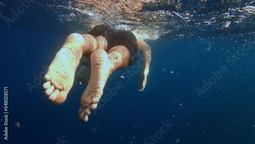 POV exploring underwater world in blue sea following a free diver swimming breast stroke. Swimmer producing many air bubbles as he is bathing in ocean. Explore wild nature. Film grain pixel texture. photo