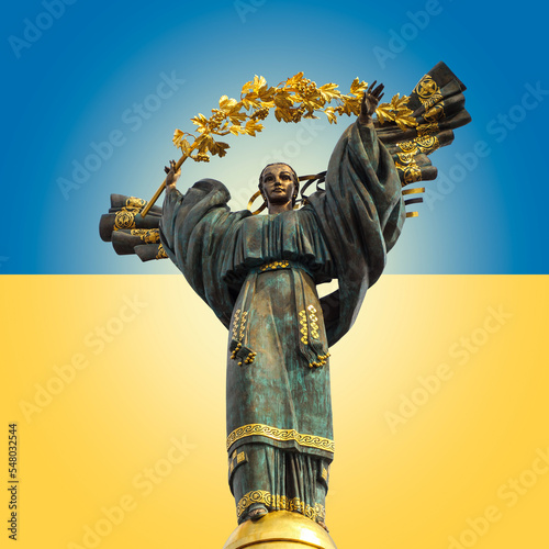 Monument of Independence of Ukraine on background of Ukrainian state flag. Memorial on Maidan Nezalezhnosti, bronze statue of ukrainian woman in national clothes on The Independence Square in Kiev. photo