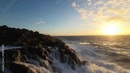 Aerial view flight very close up foamy spray waves ocean crash rocky shore by sunset rock
