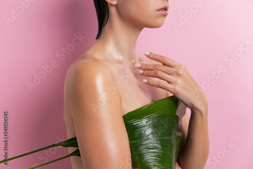 young woman covers her breasts with a green leaf of a tropical plant in summer on a pink background. ecological healthy weight loss of a person. photo