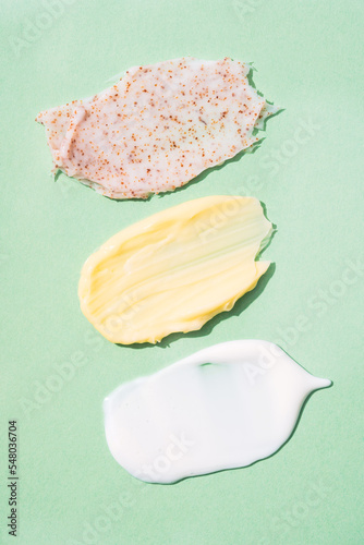 Cream and scrub smears texture. Set of cosmetic products smudges over green background. Natural skincare product. Vertical image
