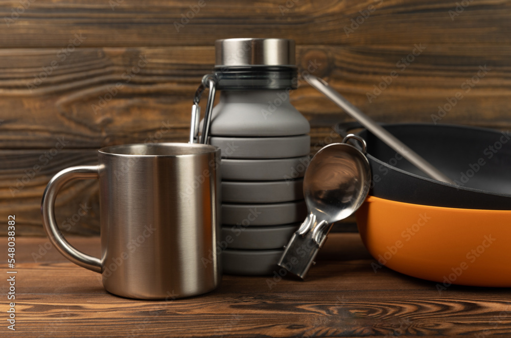 Set of travel equipment on a brown textured background. EDC set. Flat layout. Camping plate, mug, bottle, spoon and compass. Set of travel equipment on a brown textured background. EDC set. Flat layout. Camping plate, mug, bottle, spoon and compass.