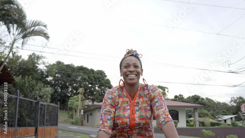 Mujer afro caribeña con una gran sonrisa montada en una bicicleta ofreciendo productos para la venta en la calle con ropa muy colorida photo
