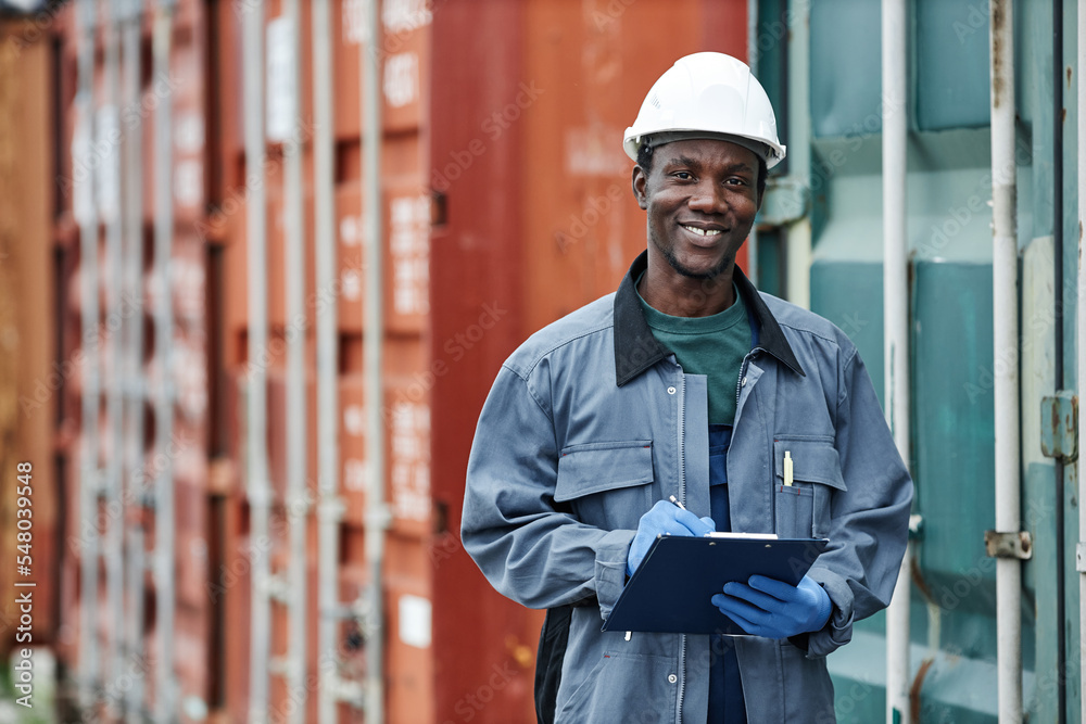 Waist up portrait of smiling young worker wearing hardhat while posing in container shipping docks, copy space Waist up portrait of smiling young worker wearing hardhat while posing in container shipping docks, copy space