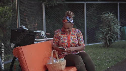 Imagen de una mujer afro caribeña sentada en el exterior tomándole fotos a una canasta con productos para la venta  en su comunidad photo