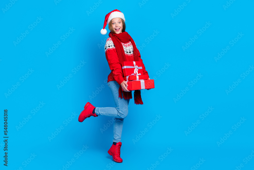 Full length photo of funny impressed school girl dressed red x-mas ornament pullover holding gifts pile stack isolated blue color background Full length photo of funny impressed school girl dressed red x-mas ornament pullover holding gifts pile stack isolated blue color background