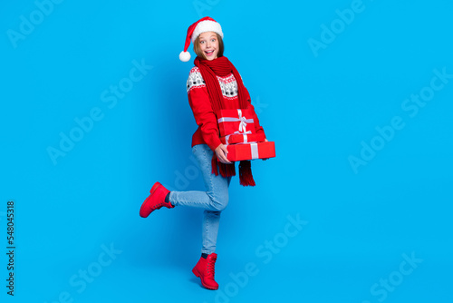 Full length photo of funny impressed school girl dressed red x-mas ornament pullover holding gifts pile stack isolated blue color background