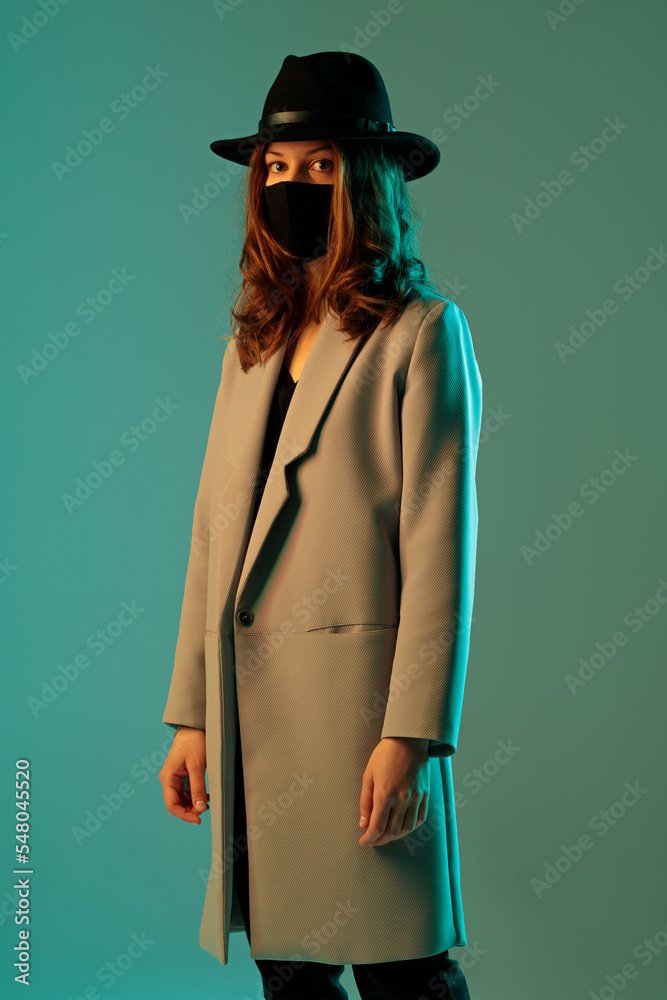 Fashionable woman in a coat, hat and protective mask on a green background.