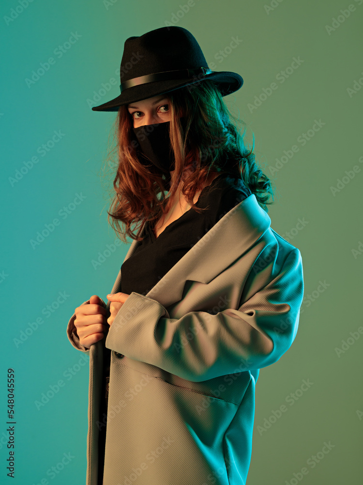 Portrait of a fashionable woman in a coat, hat and protective mask on a green background.