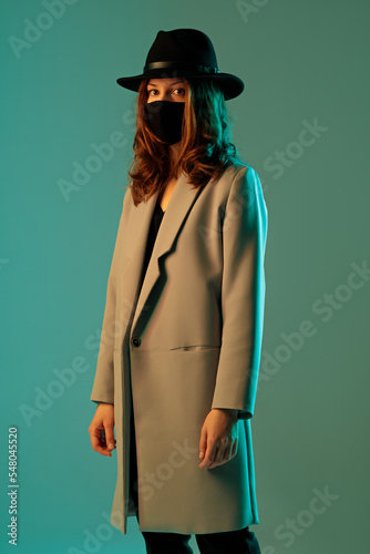 Obraz na płótnie Fashionable woman in a coat, hat and protective mask on a green background. w salonie