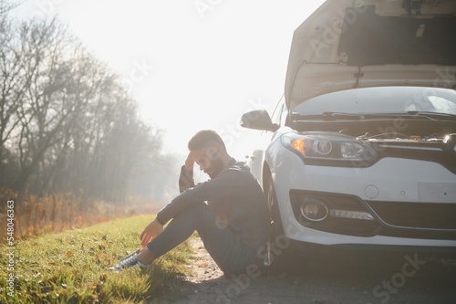 Fototapeta Naklejka Na Ścianę i Meble -  Picture of frustrated man sitting next to broken car with open hood