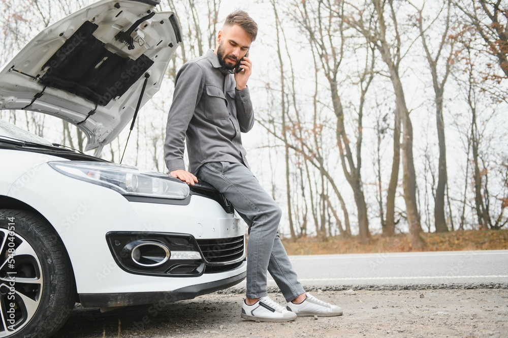 Sad driver calling car service, opening hood, having engine problem standing near broken car on the road. Car breakdown concept Sad driver calling car service, opening hood, having engine problem standing near broken car on the road. Car breakdown concept