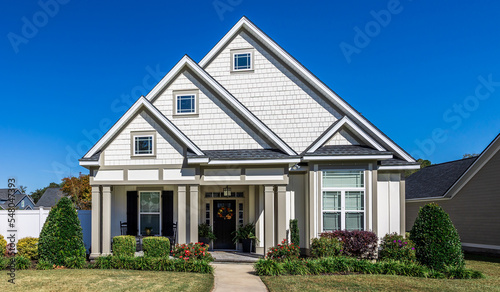 The front view of a cottage craftsman style white house with a triple pitched roof with a sidewalk, landscaping and curb appeal © Ursula Page
