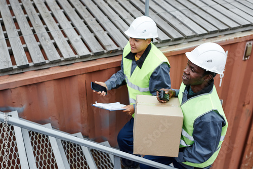 High angle portrait of two workers carrying boxes up stairs at shipping docks