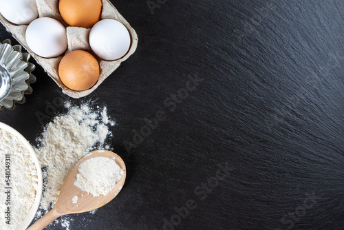 Baking cooking Ingredients background with copy space. Flour, eggs, milk, bakeware on black slate surface. Top view, flat lay. Mockup menu, banner, header for site, baking concept