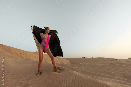 A girl in a faux fur coat in the desert. Animal protection. Ecological concept. Photographing a model in the desert. Swimsuit. Beautiful girl in heavy boots. Sand around. Hot region outdoors. Blonde 