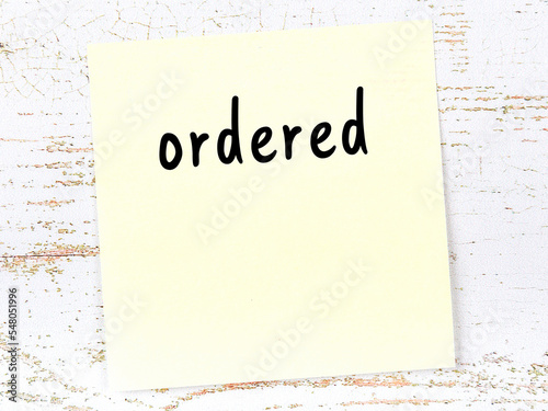 Yellow sticky note on wooden wall with handwritten word ordered