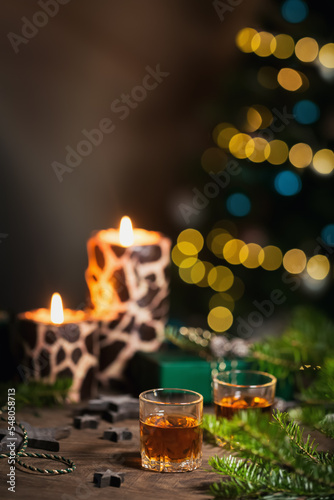 Two shot glasses of whiskey or bourbon with Holiday decoration on wooden background. New Year  Christmas and winter holidays whiskey mood concept