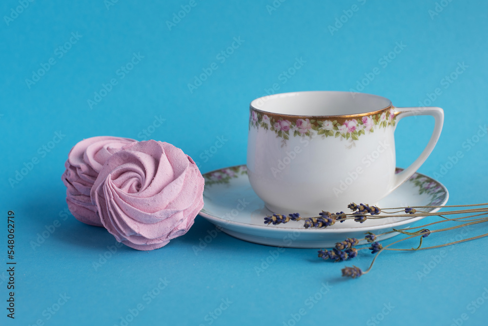 Homemade pink zephyr or marshmallow with white porcelain cup and lavander close to. Isolated on blue background. Sweet Meringue dessert. Valentine’s or Mothers Day concept. Homemade pink zephyr or marshmallow with white porcelain cup and lavander close to. Isolated on blue background. Sweet Meringue dessert. Valentine’s or Mothers Day concept.