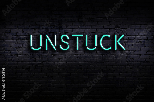 Night view of neon sign on brick wall with inscription unstuck