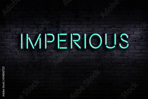 Neon sign. Word imperious against brick wall. Night view photo