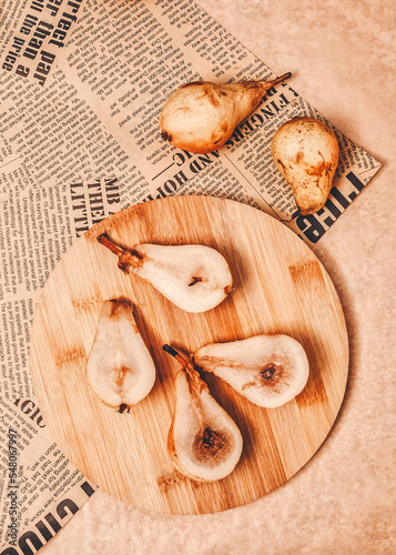 Rustic autumn concept. Retro, vintage idea. Juicy pears were cut in half and placed on a wooden bamboo board. Newspaper as decoration. Warm color tones, sharp edges of objects. Flat lay concept. photo